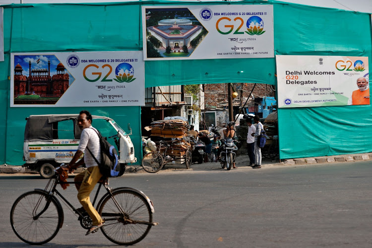 A man rides a bicycle past hoardings installed on plastic sheeting placed to screen a slum area alongside a road ahead of the G20 Summit in New Delhi, India, September 7, 2023.