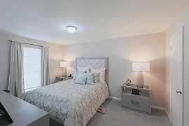 Model bedroom with neutral walls and carpet with light trim and doors with a window with blinds on the left wall.