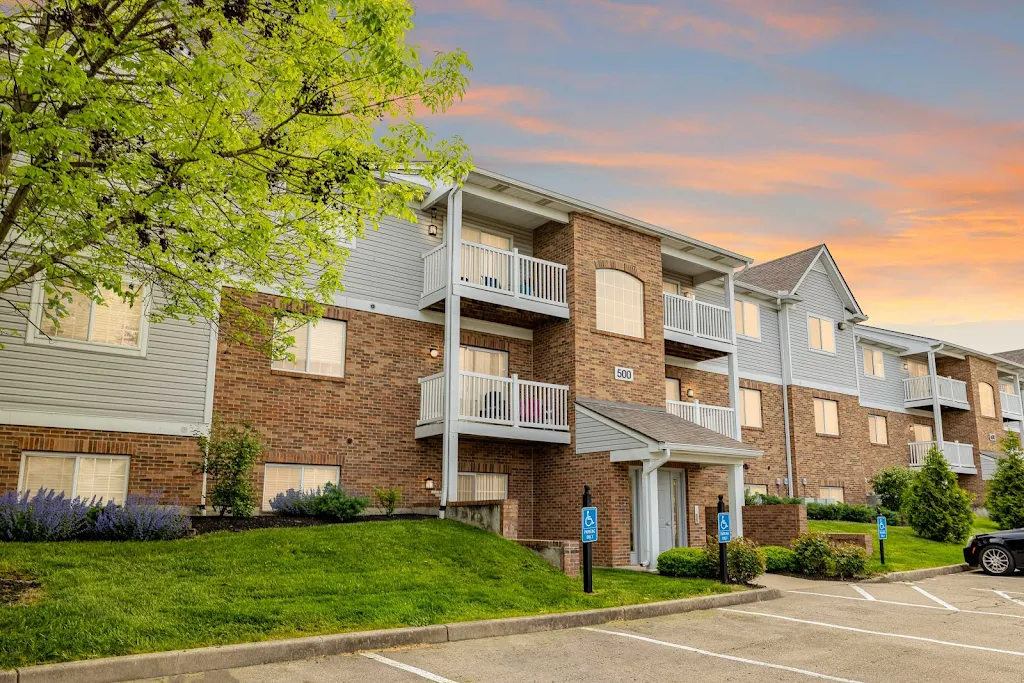 Brick apartment complex with white balconies, green lawn, and sunset sky.