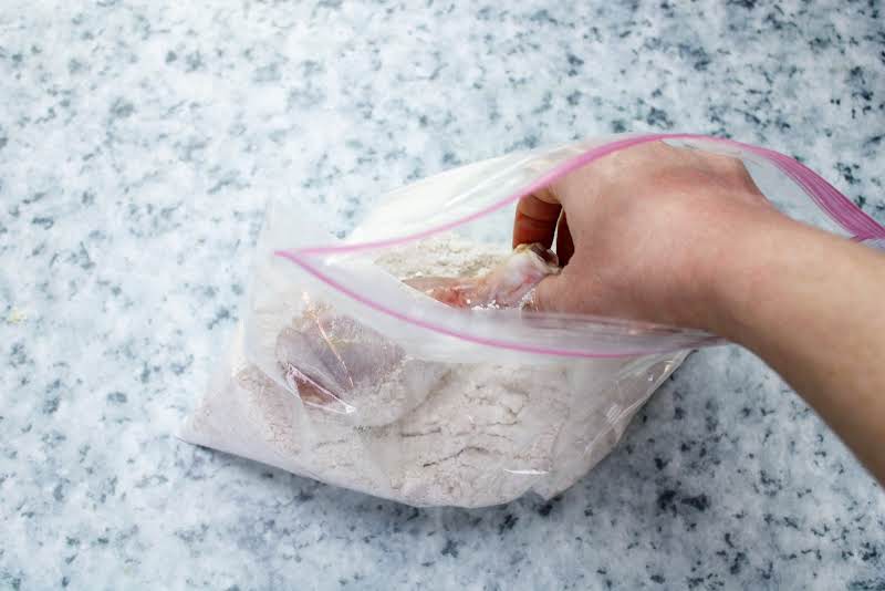 Placing Chicken In A Resealable Bag With Seasoned Flour.