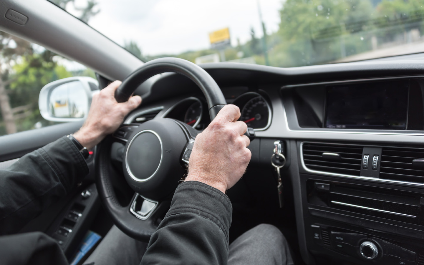 man's hands holding car steering wheel