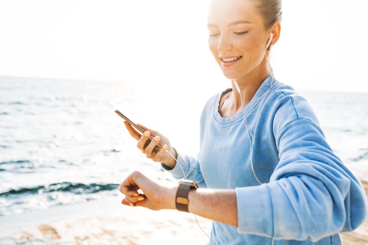 Woman runs on the beach looking at Apple Watch with headphones in