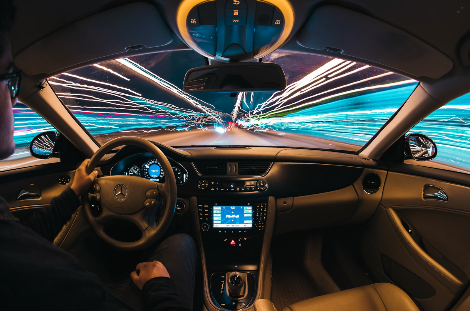 The inside of a Mercedes with a man driving it and holding onto the wheel with one hand.