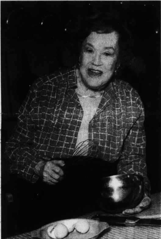 Image of an elderly woman looking at camera holding a whisk and a dish.
