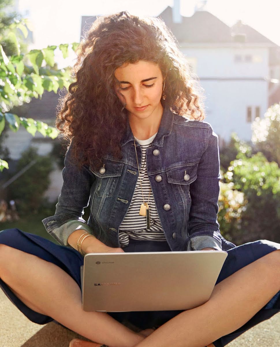 Una mujer usando un Chromebook de Google sentada al aire libre.