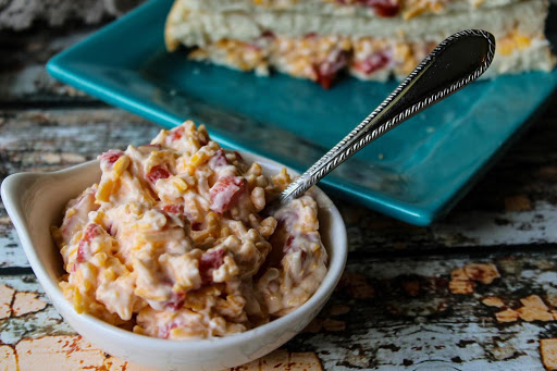 A bowl of pimento cheese with a sandwich in the background.