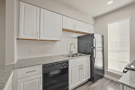 Modern apartment kitchen with white cabinets, black appliances, and granite countertops.