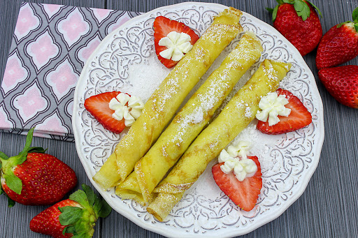 Norwegian pancakes rolled on a plate with strawberries and whipped cream.