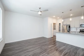 Open concept living room with wood-inspired flooring, white walls, ceiling fan, and access to the kitchen