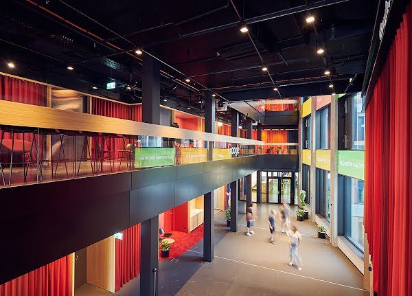 La vista dall'alto dell'atrio della centrale Google di Zurigo mostra gli spazi aperti dell'architettura. Le portefinestre sono alte e al primo piano vediamo un porticato sorretto da colonne. Al piano terra camminano alcuni collaboratori.