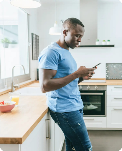 A person stands in a kitchen looking down at a smartphone.