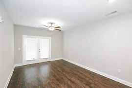 Living area with wood inspired flooring, patio door and window, and ceiling fan with light fixture.