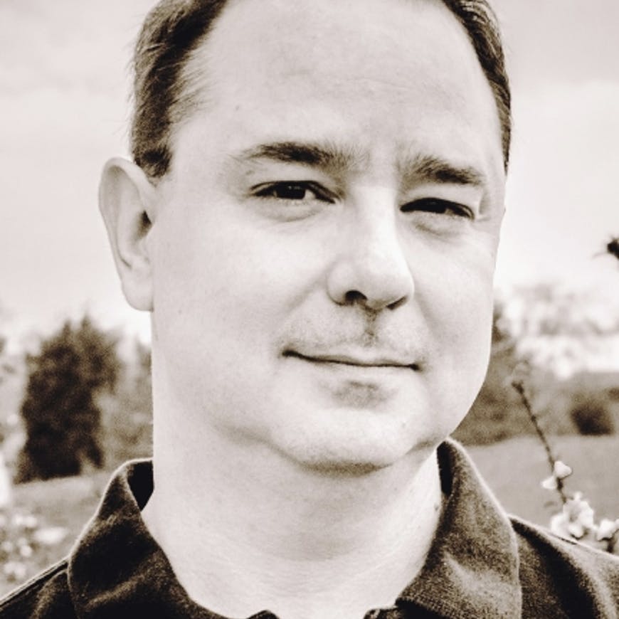 This is John Scalzi's author photo. Scalzi is a white man; in this photo, his hair is short and he is wearing a collared shirt.