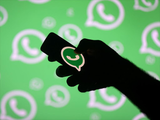 A man poses with a smartphone in front of displayed Whatsapp logo in this illustration.