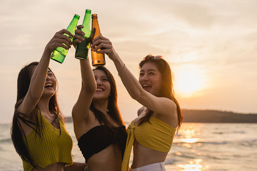 three women toasting with beer bottles on the beach