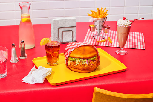 In a diner set, there is a tray with a large hamburger-shaped cake on it.