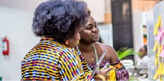 Two women working with post-it notes on a whiteboard, smiling