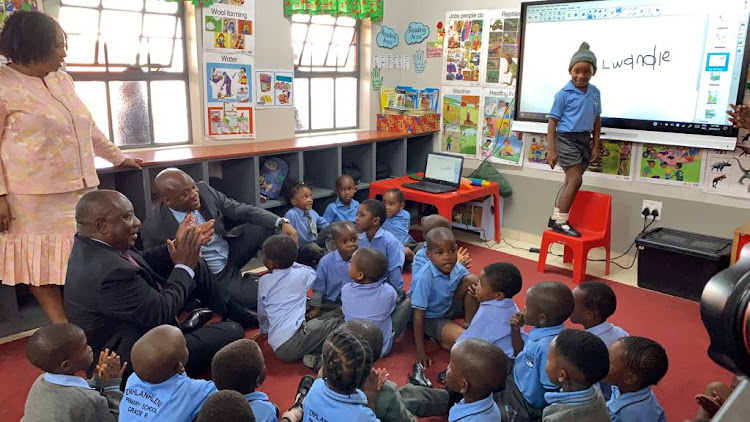 President Cyril Ramaphosa sits with Grade R pupils while Lwandle Nxumalo, 6, writes his name on a new smartboard.