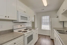 A modern kitchen in an apartment with white cabinets, stainless steel appliances, and gray countertops.