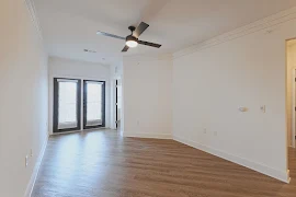 Living room with double window doors leading to balcony, black ceiling fan, white walls and trim, plank flooring