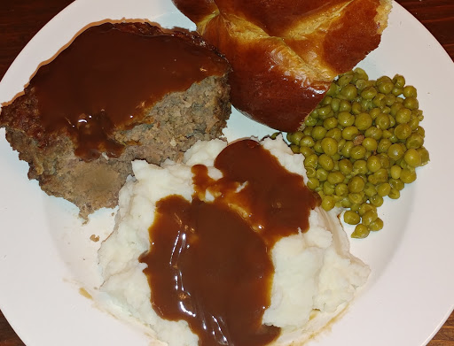 Tomato-free meatloaf with mashed potatoes, beef gravy, buttered peas, and warm bread.