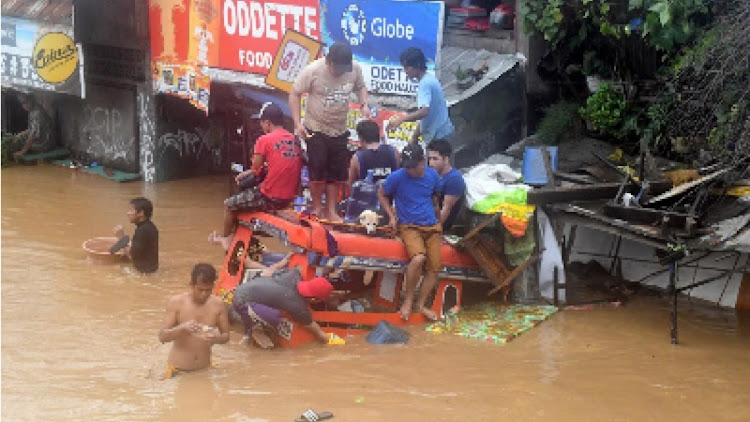 Residents are seen on the top of a partially submerged vehicle along a flooded road in Cagayan de Oro city in the Philippines. REUTERS/Froilan Gallardo