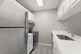 Modern apartment kitchen with stainless steel appliances, white cabinets, and white countertops.