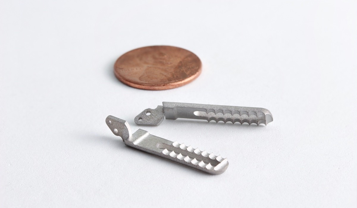 A pair of tiny prototype grippers for a laparoscopic surgical tool next to a penny, which is roughly the same size as them.