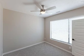 Bedroom with grey walls and grey carpet and on the right wall is a large window with white blinds.