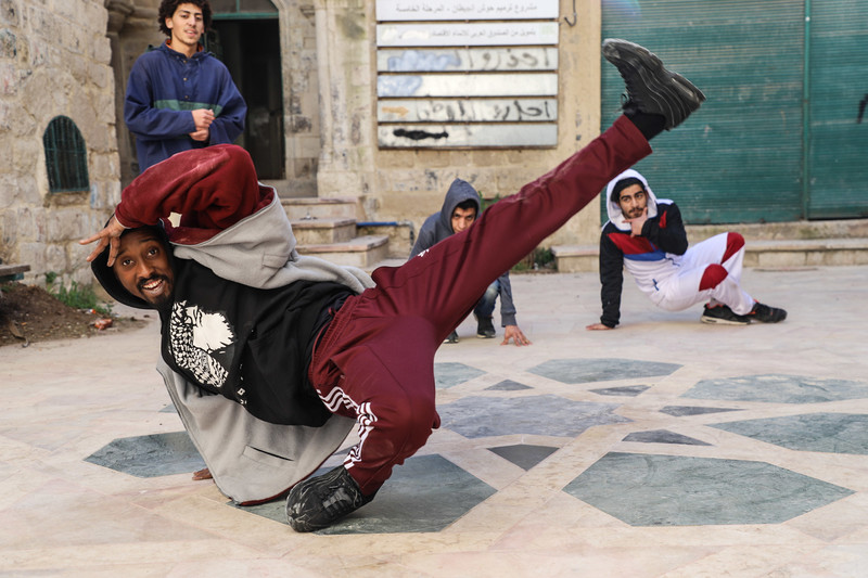 Man does breakdance move surrounded by three onlookers. 