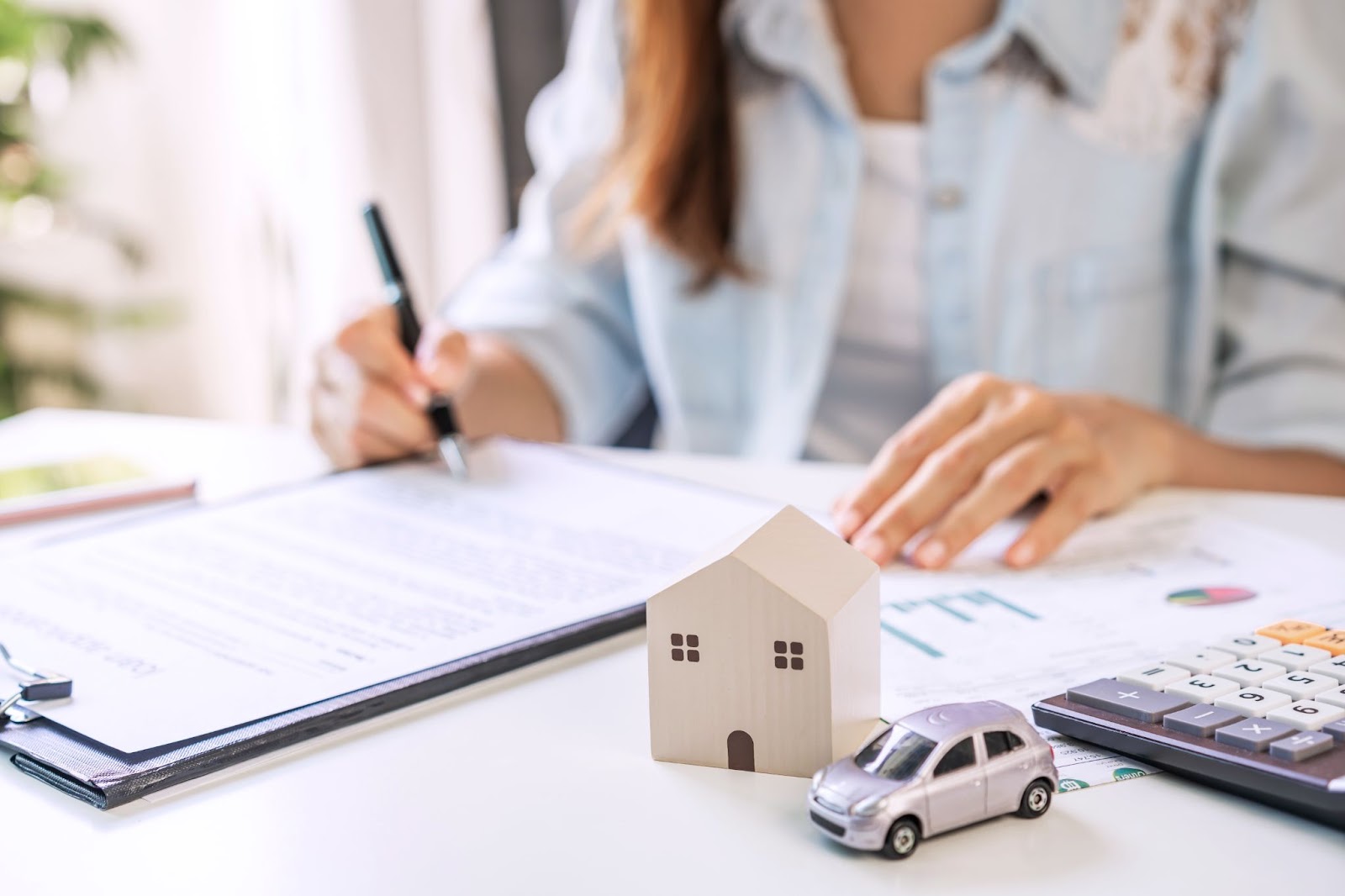 woman signing contract next to model of house and car