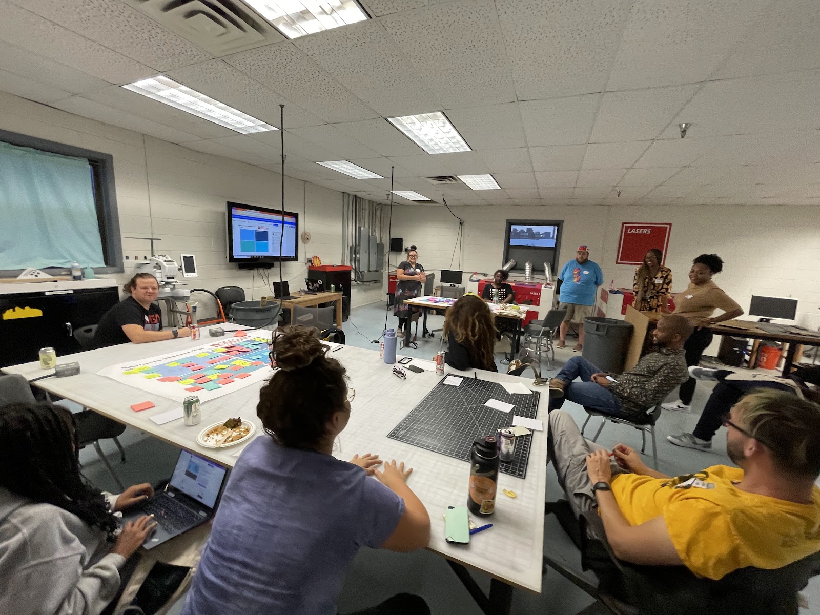 Educators and community members sit around work tables in the community makerspace Protohaven watching a slideshow presentation on Maker Learning given by Nina Barbuto. 