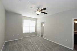 Neutral carpeting in walls in bedroom with window, walk-in closet, ceiling fan with light fixture, and attached bathroom