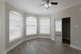 Bedroom with wood plank flooring, mirrored closet door, three arched windows, ceiling fan, and light gray walls