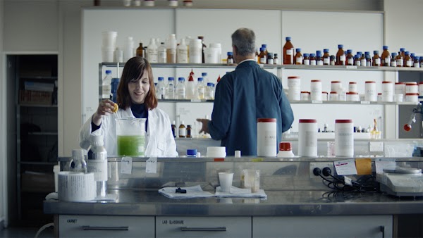 Brianne West, founder of Ethique, prepares a solution in her cosmetics lab. She has red hair and wears a lab coat.