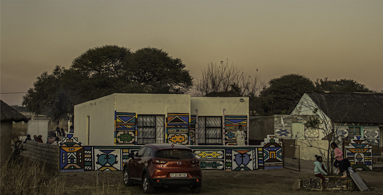 A homestead of the Msiza family, occupied by Siyabonga's grandmother, and the venue of the Wela homecoming celebration. In the old days, if you had a son at the Wela, you had to repaint your house (various muds created the different colours, but today they have been replaced by commercial paints). A white flag denotes the home of an initiate.