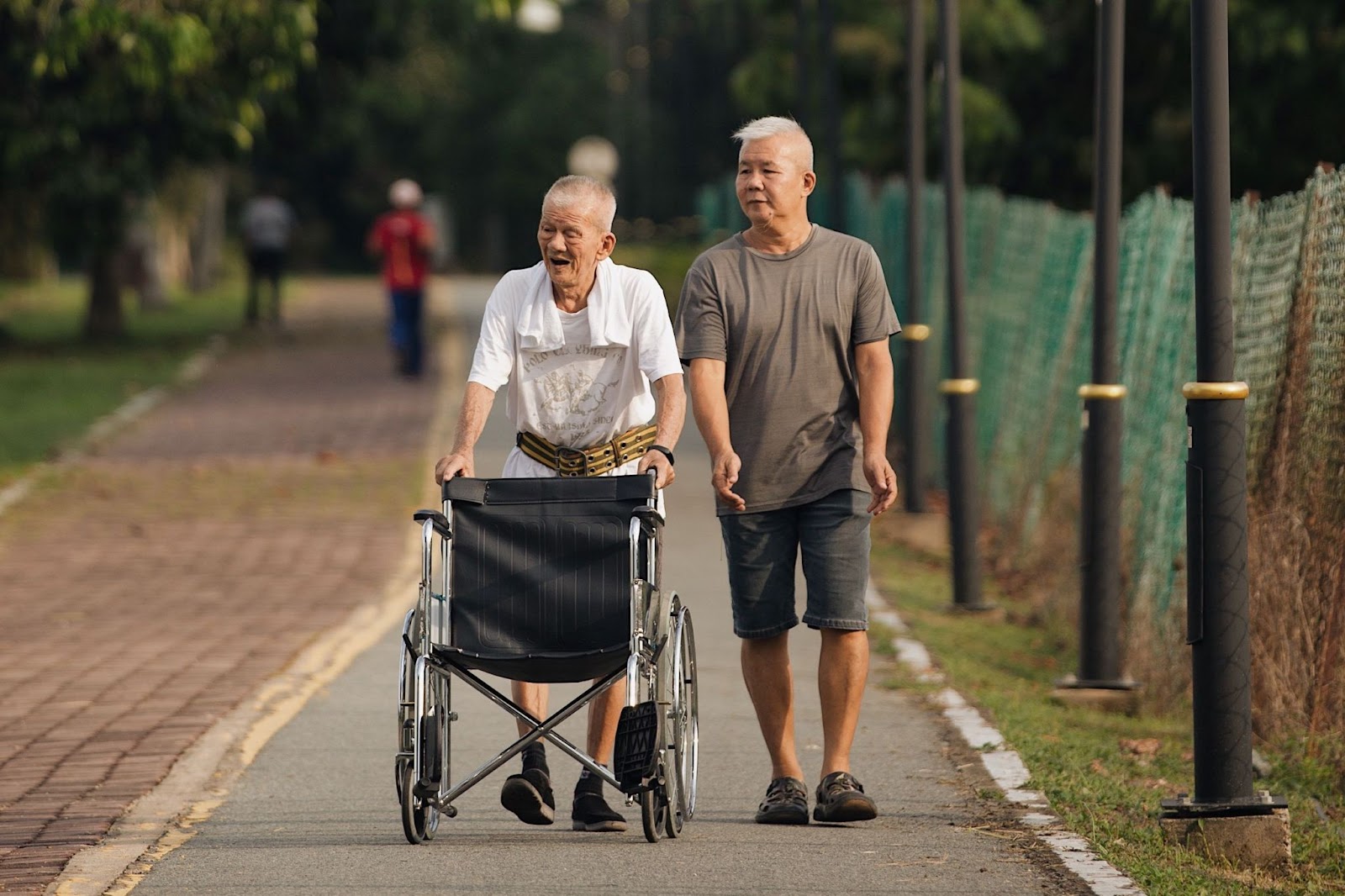 Older-man-with-wheelchair-and-younger-man-walking-in-park