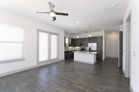 Living room with wood-inspired flooring, light walls, ceiling fan, and patio door. Kitchen with stainless steel appliances