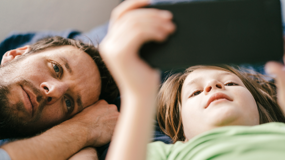 Padre e hijo mirando un teléfono celular mientras están acostados