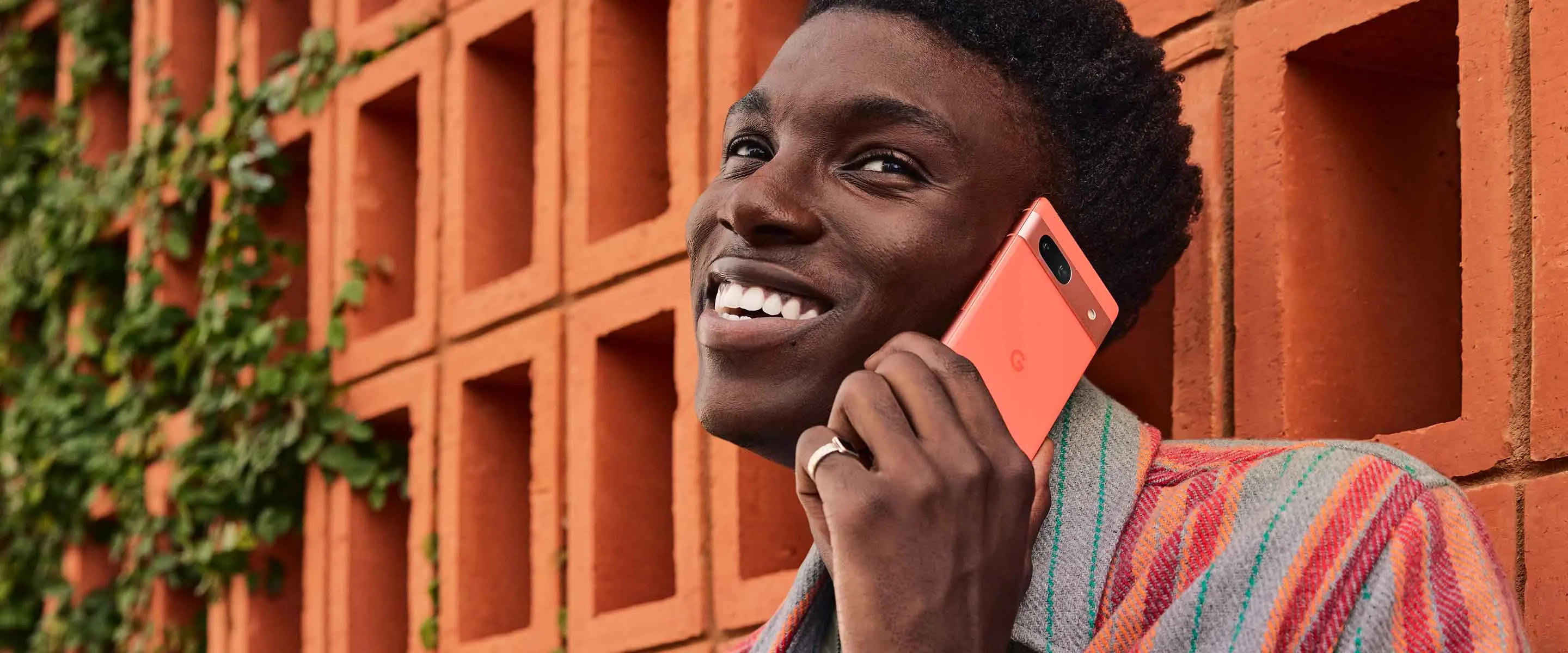 Person using Google Pixel 7a to take a call while smiling and leaning on an orange wall