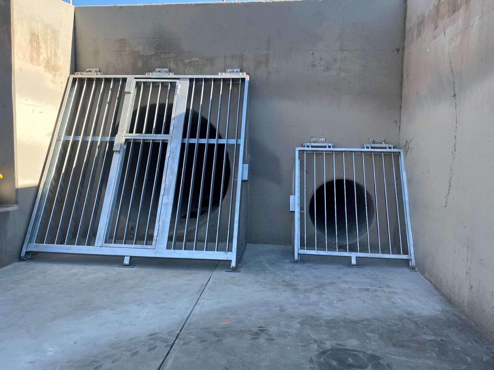 A photo of a large outlet and a small outlet of a storm drain, covered by nice new metal gates.