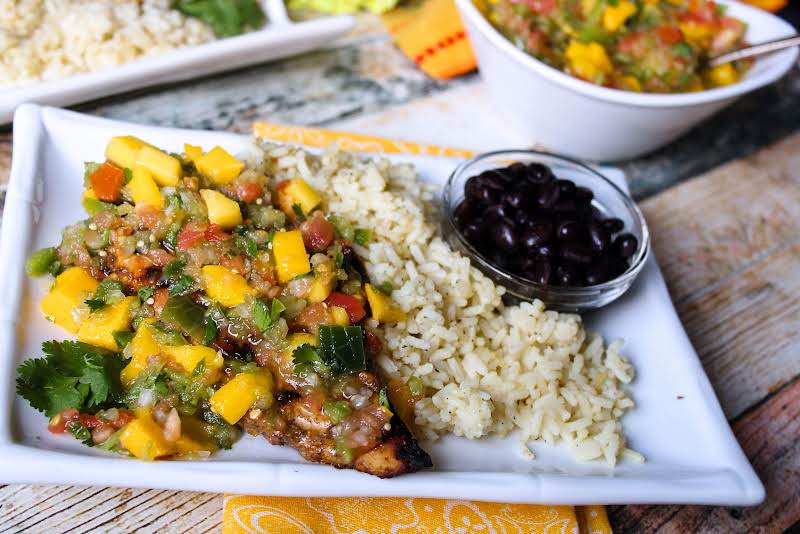 Grilled Jerk Chicken With Mango Salsa On A Plate With Rice And Beans.