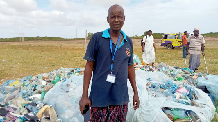 Mokowe Mainland Community-Based Organization chairperson Abdirashi Aden stands next to a pile of plastic bottles collected from beaches and shores in Lamu.