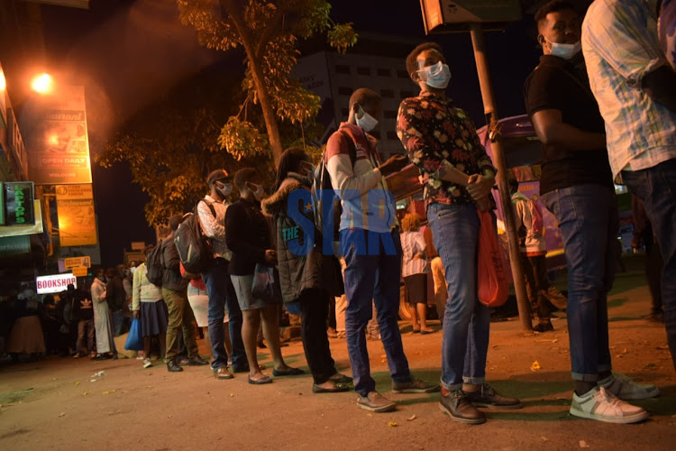 Commuters line up along Moi Avenue as they await Pblic transport for Donholm area an hour before curfew on. April 21/