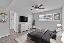 Model bedroom with wood-inspired flooring, window with blinds, and door to the bathroom 