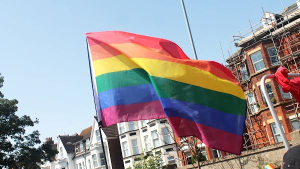 Una bandera de arcoíris del Orgullo ondea al viento al ser llevada por una calle en un desfile.