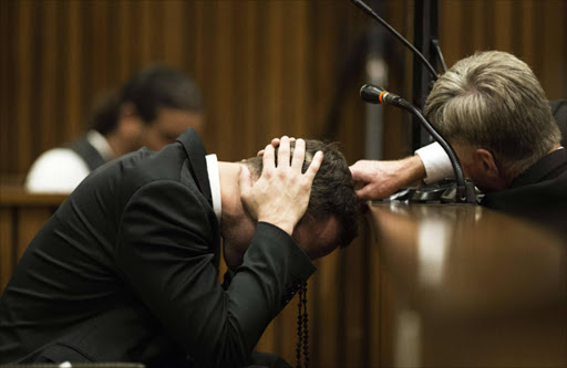 A member of his legal team reaches out to South African Paralympic athlete Oscar Pistorius (L) as he covers his ears with his hands while a witness gives testimony and recounts the night of the crime during the fourth day of his trial for the murder of his girlfriend Reeva Steenkamp at the North Gauteng High Court in Pretoria on March 6, 2014. AFP PHOTO / POOL / MARCO LONGARI