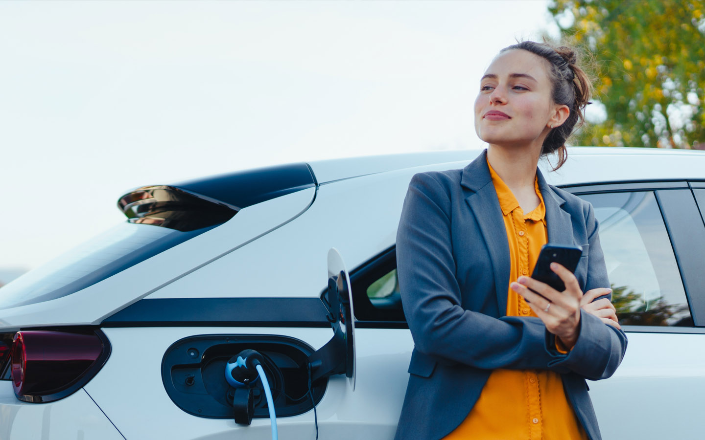 woman using phone while her car is charging. follow the tips to avoid common hybrid car problems and enjoy a hassle free hybrid car experience. 