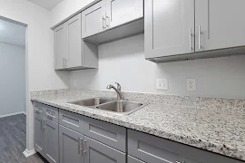 Modern kitchen with gray cabinets, granite countertops, and stainless steel sink in an apartment.