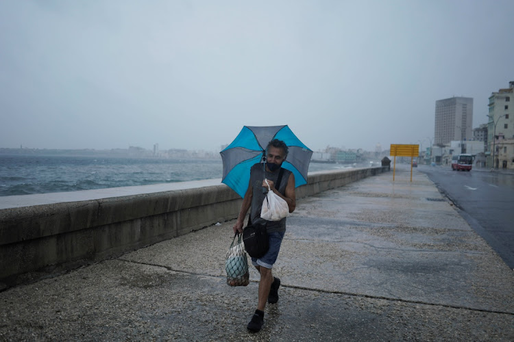 A man protects himself from wind and rain as he walks at the seafront Malecon while Hurricane Ida approaches the island, in Havana, Cuba on August 27, 2021.